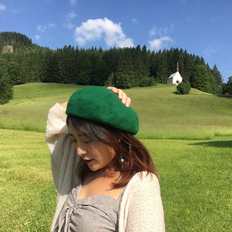 Melody Zhao in a green beret against a scenic mountain landscape